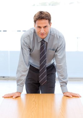 Confident businessman posing leaning on a table clipart