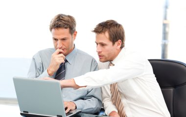 Two handsome businessmen working together on a project sitting a clipart