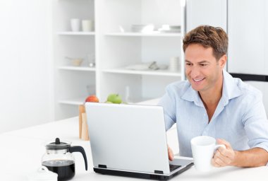 Happy man working on his laptop while drinking coffee clipart