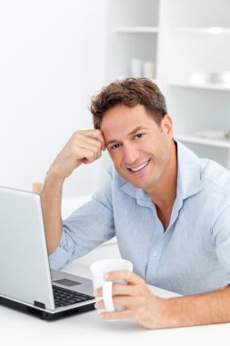 Portrait of man drinking coffee while working on his laptop clipart