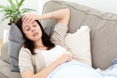 Indisposed woman feeling her temperature while resting on the so clipart
