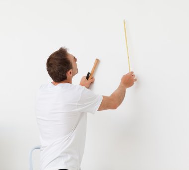 Handsome man looking at a wall with ruler and tools clipart