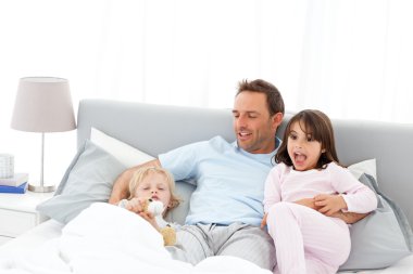 Handsome man with lying on his bed with his children at waiking clipart