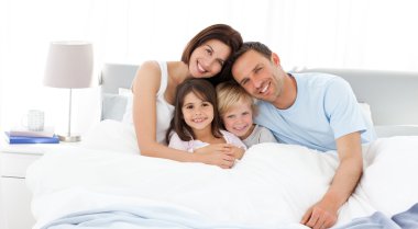 Happy children with their parents on the bed clipart