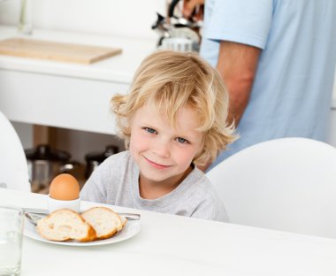 Little boy eating boiled egg and bread at breakfast clipart