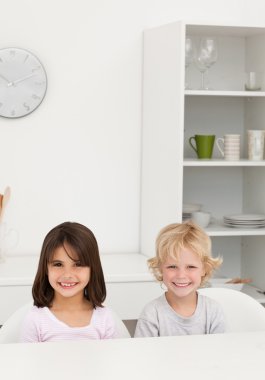 Little brother and sister smiling sitting at a table in the kitc clipart