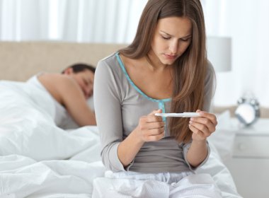 Pretty woman looking a pregnancy test while her boyfriend sleepi clipart