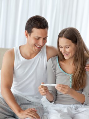 Happy couple looking at a pregnancy test on their bed clipart