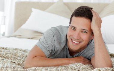 Joyful man lying on th edge of his bed at home clipart