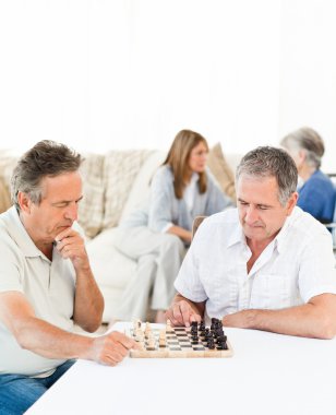 Men playing chess while their wifes are talking clipart