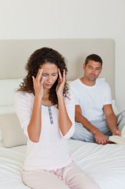 Woman having a headache while her husband is reading clipart