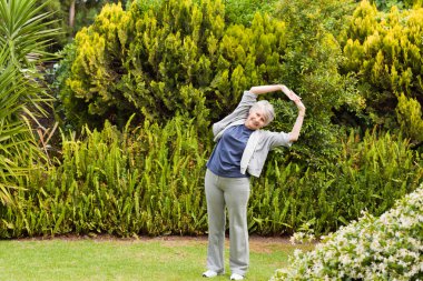 Retired woman doing her streches in the garden clipart