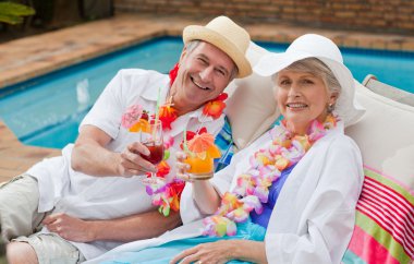 Mature couple drinking a cocktail beside the swimming pool clipart