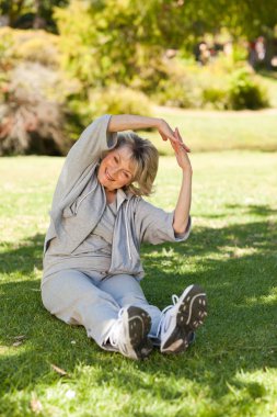 Senior woman doing her streches in the park clipart