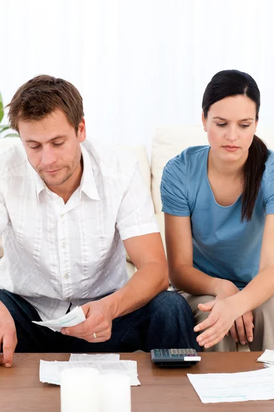 Desperate couple looking at their bills sitting on the sofa — Stock Photo, Image