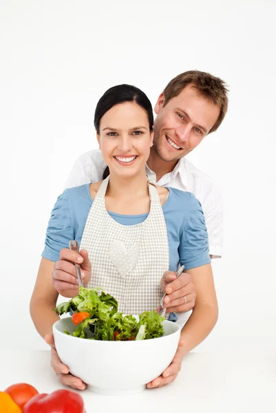 Happy man mixing a salad with his girlfriend in the kitchen — Stock Photo, Image