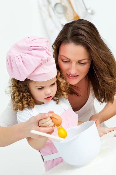 Mother and daughter breaking eggs while cooking — Stock Photo, Image