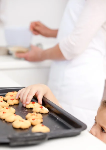 Χαριτωμένο μικρό κορίτσι λαμβάνοντας τα cookies, ενώ η μητέρα της είναι το μαγείρεμα — Φωτογραφία Αρχείου