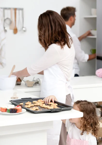 Schattig klein meisje nemen cookies terwijl haar ouders zijn koken — Stockfoto