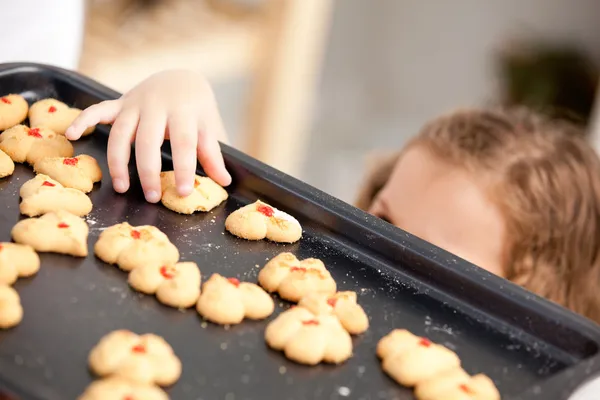 Acercamiento de una niña pequeña tomando una galleta detrás de la ba de su madre — Foto de Stock