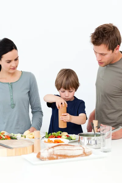 Schattige jongen zetten zout en peper in zijn salade in de keuken — Stockfoto