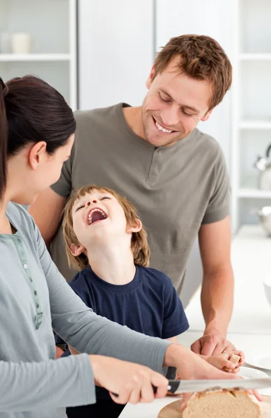 Kleine jongen lachen terwijl zijn moeder snijden brood — Stockfoto