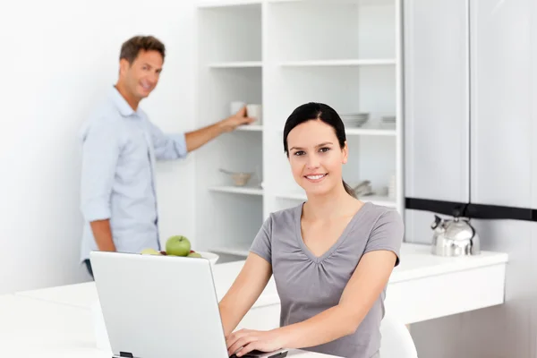 Šťastná žena v přenosném počítači, zatímco její manžel Příprava kávy — Stock fotografie