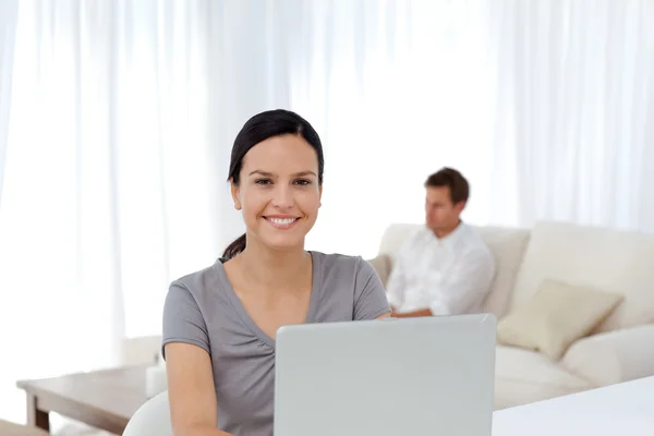 Ładny kobieta pracuje na laptopie podczas gdy jej mąż relaksujący — Zdjęcie stockowe