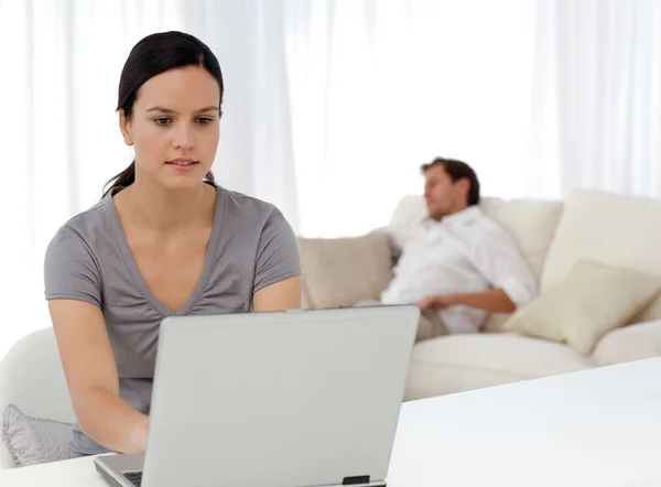Mulher atenta trabalhando no laptop enquanto seu namorado é sle — Fotografia de Stock