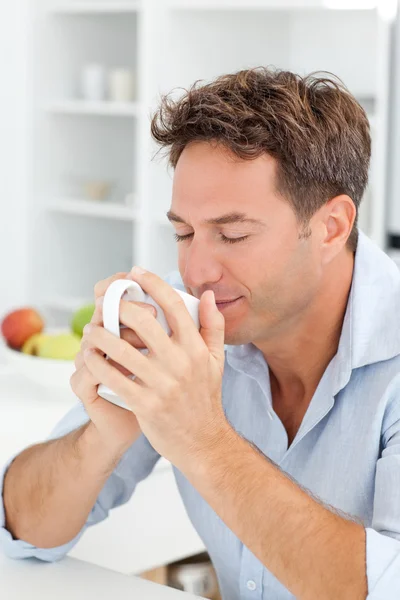 Handsome man smelling his coffee sitting in his kitchen — Stock Photo, Image