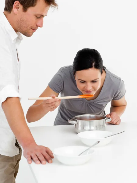 Cute woman tasting her soup with her husband in the kitchen — Stock Photo, Image