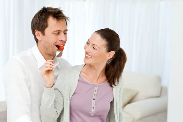 Homem feliz provando um tomate enquanto sua namorada prepara o almoço — Fotografia de Stock