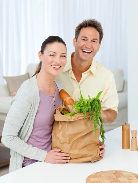 Couple laughing standing in the kitchen with shopping bags — Stock Photo, Image
