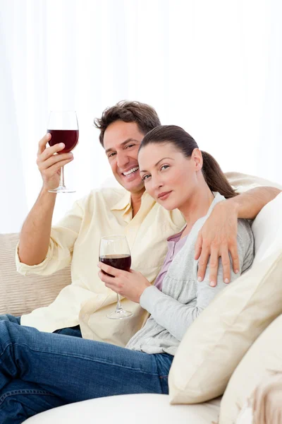 Felice coppia godendo i loro bicchieri di vino rosso sul divano — Foto Stock