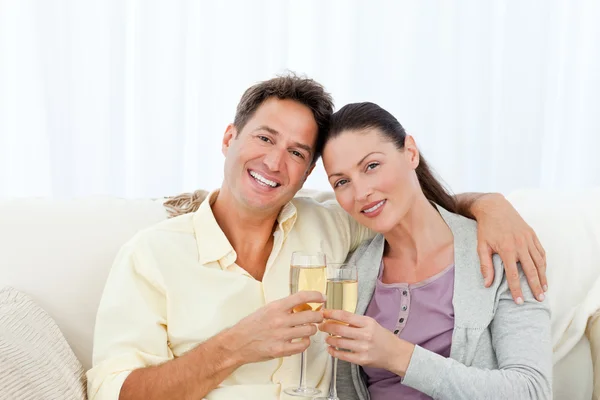 Retrato de um casal segurando flautas de champanhe no sofá — Fotografia de Stock
