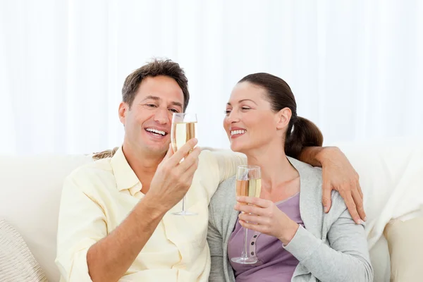 Šťastný pár, ochutnávka šampaňského sedí na pohovce — Stock fotografie