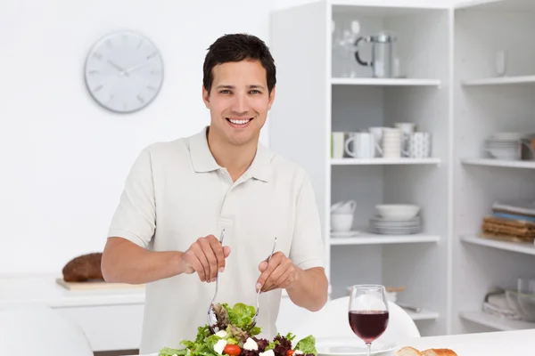Happy man preparing a salad while drinking red wine — Stock Photo, Image