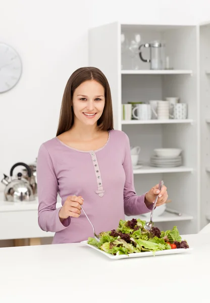 Mulher bonito misturando uma salada de pé na cozinha — Fotografia de Stock