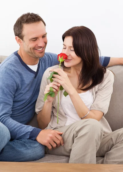 Милая женщина, чувствующая запах красной розы, расслабляясь на диване — стоковое фото