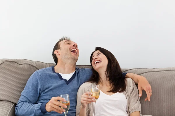 Пара смеется, когда пьет шампанское на диване — стоковое фото