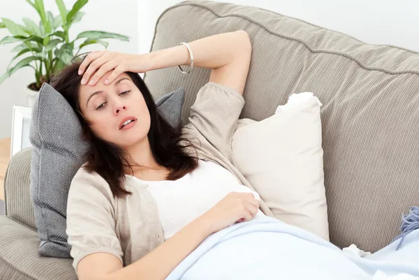 Indisposed woman feeling her temperature while resting on the so — Stock Photo, Image