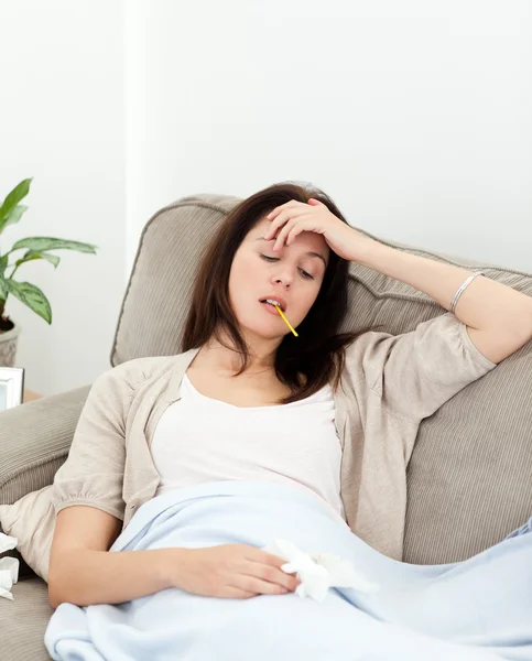 Хвора жінка приймає температуру з термометром на дивані — стокове фото