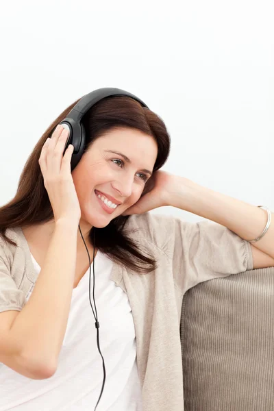 Женщина улыбается, слушая музыку на диване — стоковое фото