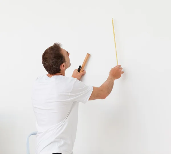 Handsome man looking at a wall with ruler and tools — Stock Photo, Image