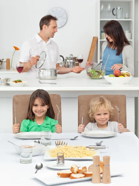 Irmão e irmã brincando com garfos enquanto seus pais cozinham — Fotografia de Stock