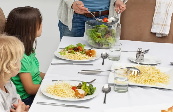 Mamma serverar sallad till hennes barn vid lunch — Stockfoto