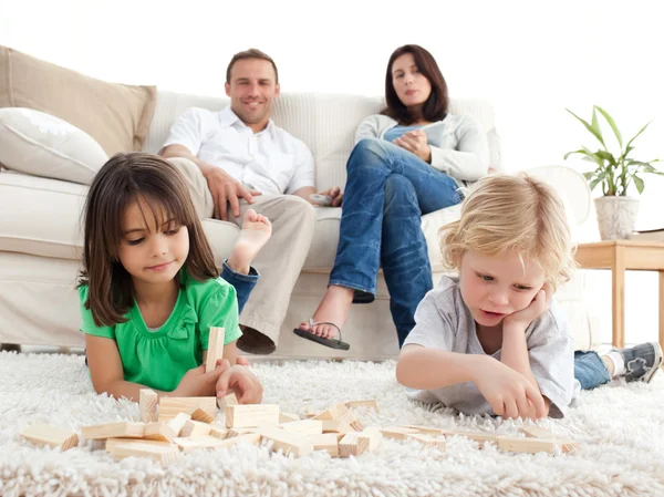 Orgulhosos pais olhando para seus filhos brincando com dominós em — Fotografia de Stock