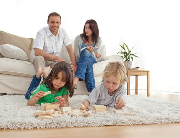 Glückliche Eltern auf dem Sofa, die ihre Kinder beim Spielen anschauen — Stockfoto