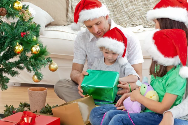 Família feliz olhando para o menino abrindo uma prese de Natal — Fotografia de Stock