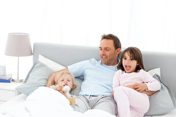 Pohledný muž leží na posteli se svými dětmi na waiking — Stock fotografie